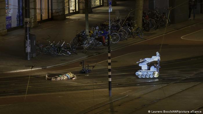Um homem camuflado está deitado ao lado de um robô policial na rua